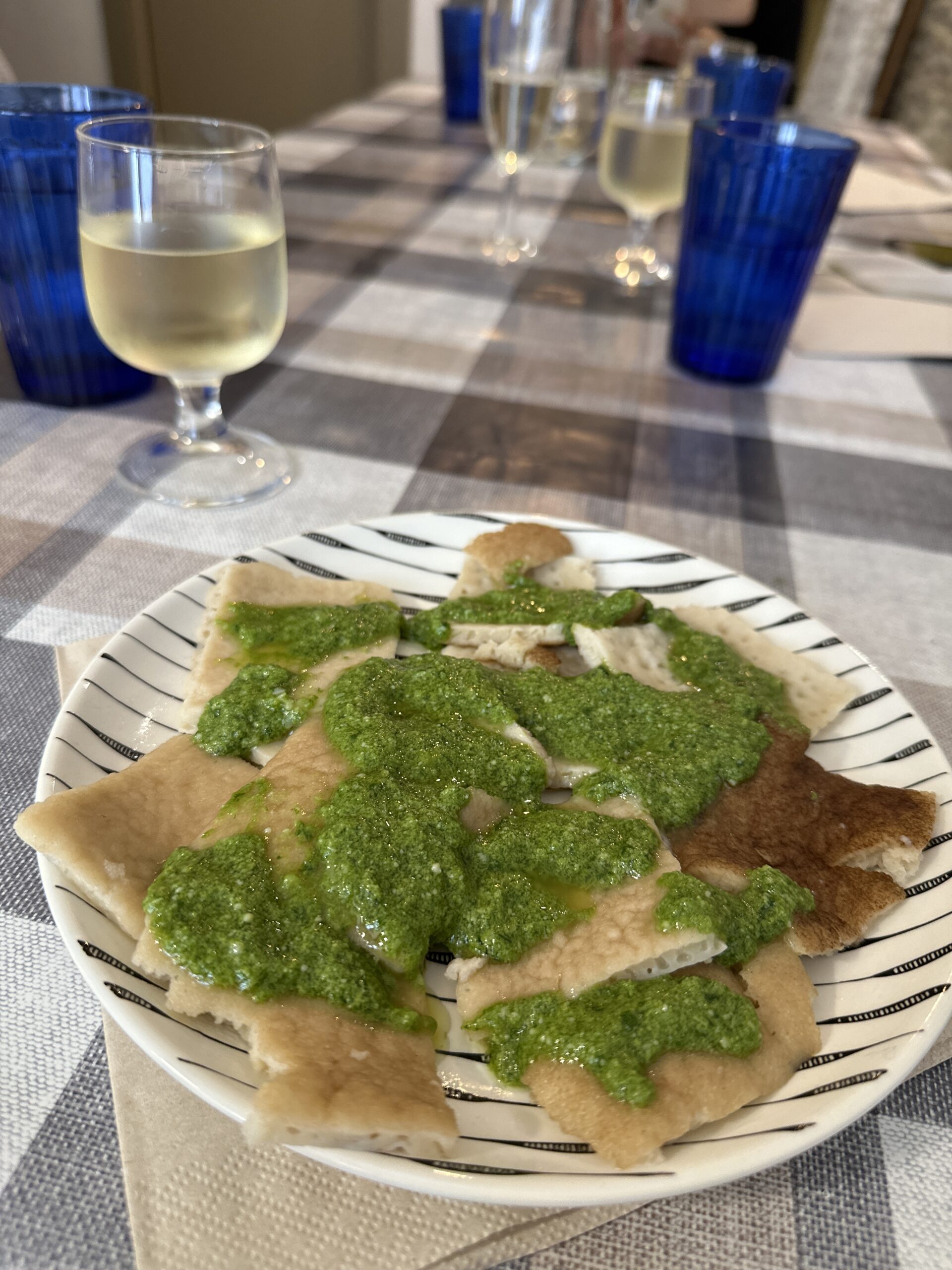 a plate has testaroli and pesto on top of it.  A glass of prosecco is next to the dish.